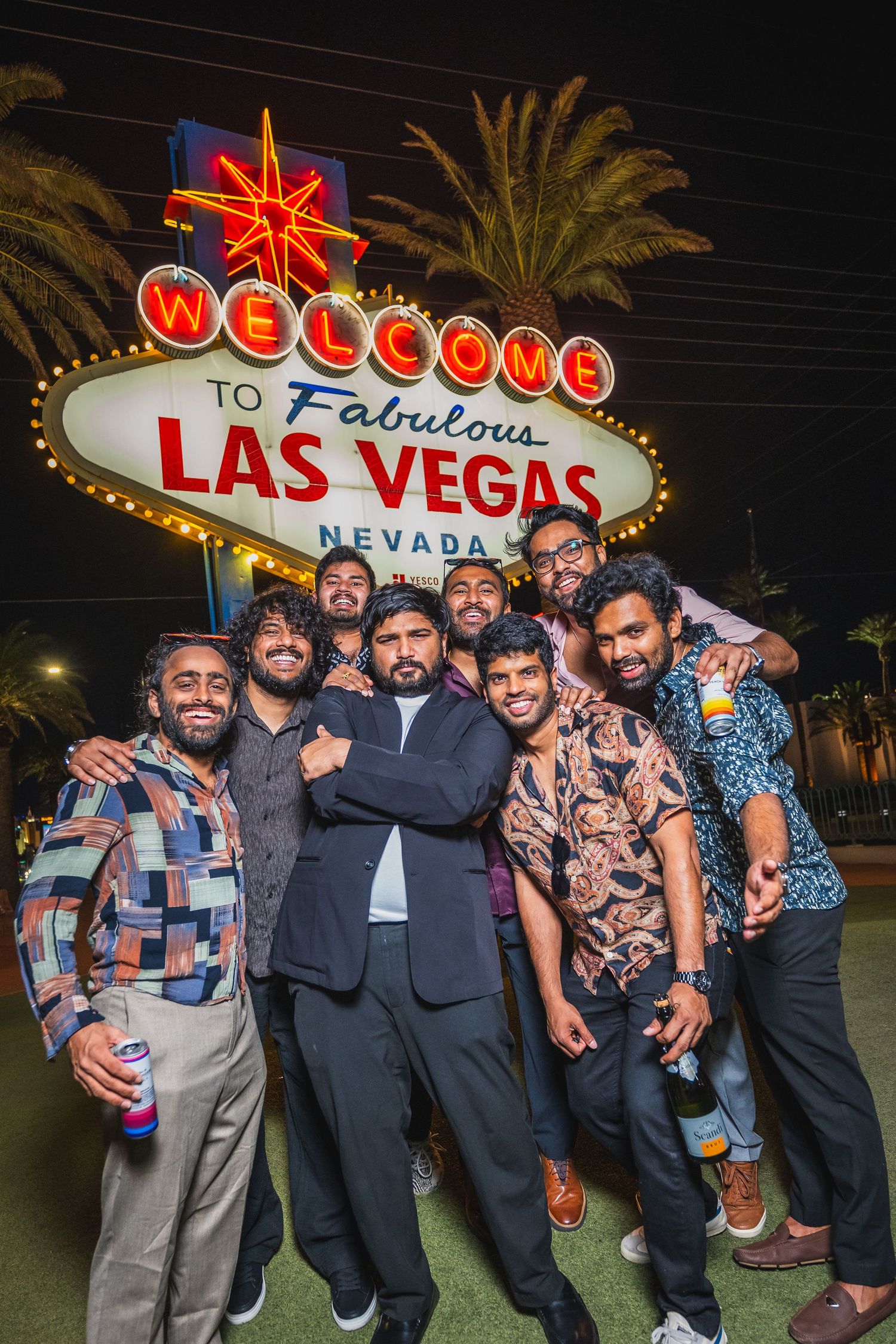 Group of men posing together in front of the Las Vegas welcome sign at night.