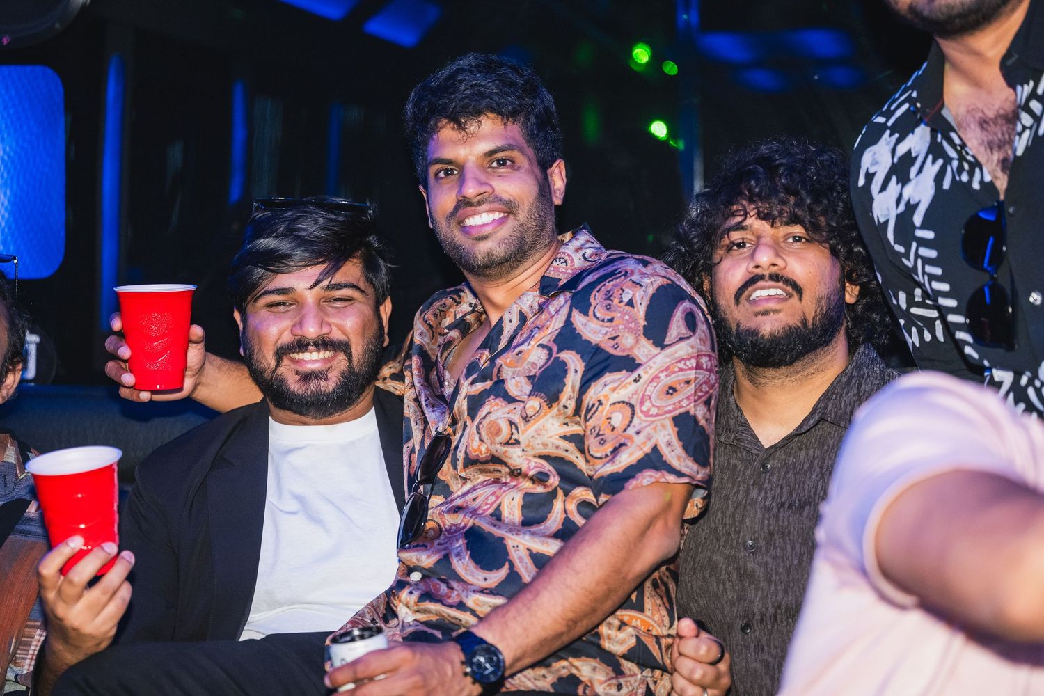 Three men smiling and posing together at a party with blue ambient lighting.