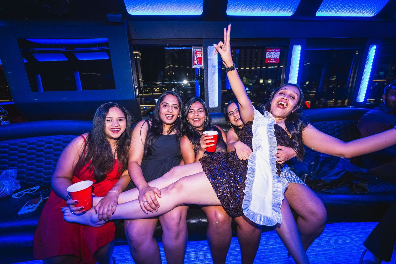 Five women smiling and celebrating together on a party bus with blue LED lighting.