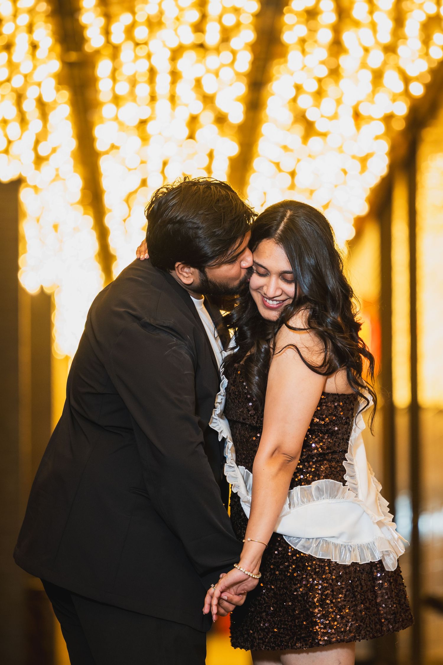 Couple sharing a tender kiss under glowing golden string lights in a romantic setting.