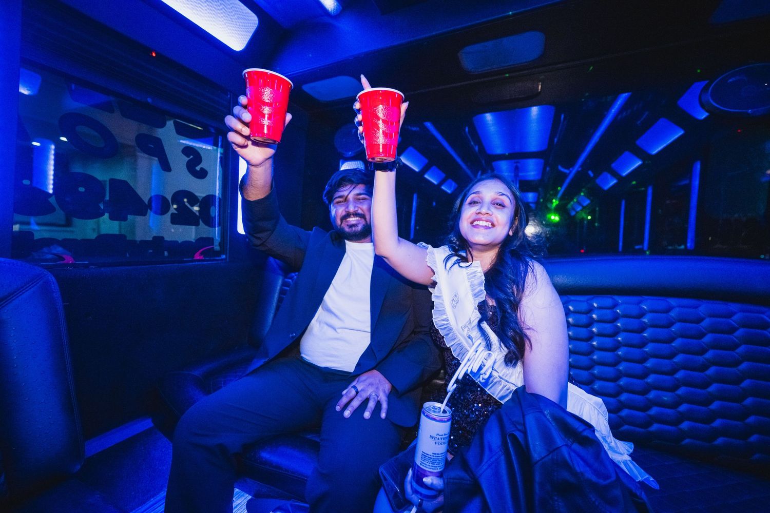 Couple celebrating on a party bus raising red solo cups in a toast under blue lights.