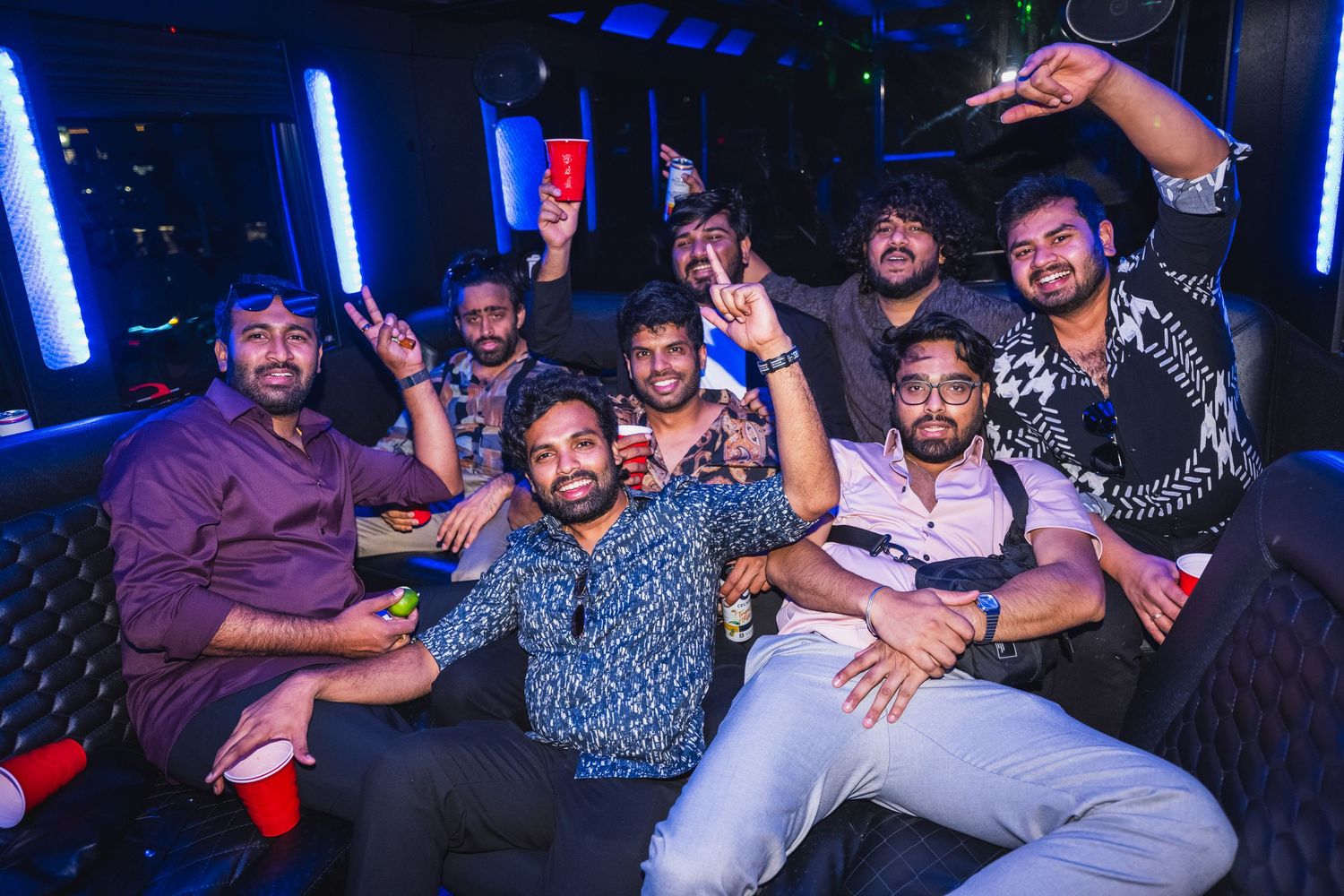 Large group of men posing and celebrating together inside a neon-lit party bus.