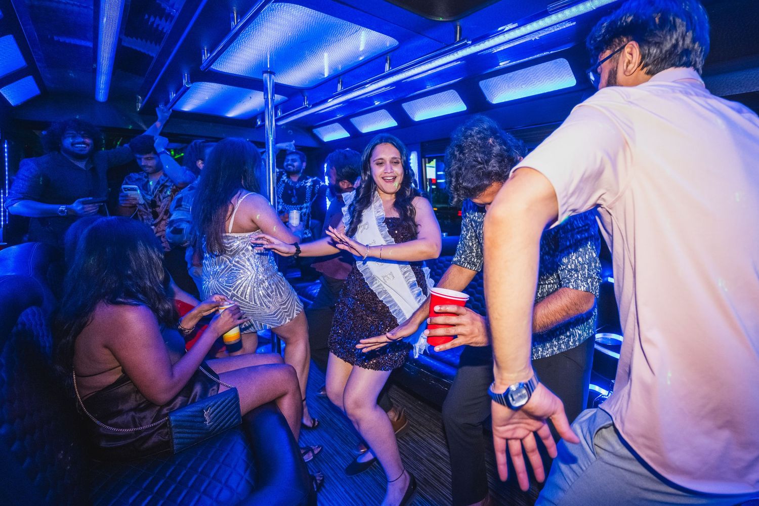 People dancing and celebrating inside a party bus with blue neon lights in Las Vegas.