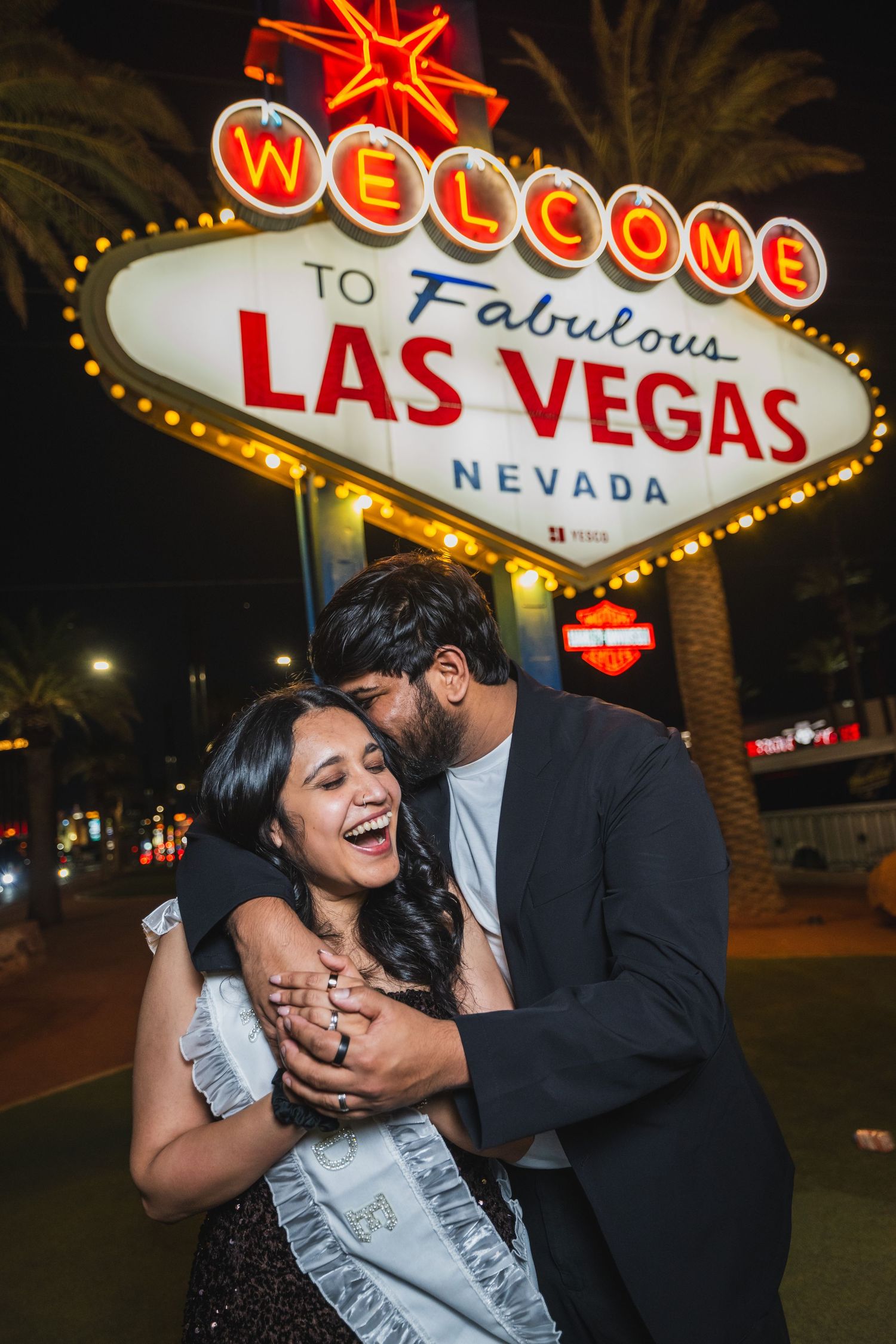 Joyful couple sharing a kiss in front of the glowing Welcome to Fabulous Las Vegas sign.