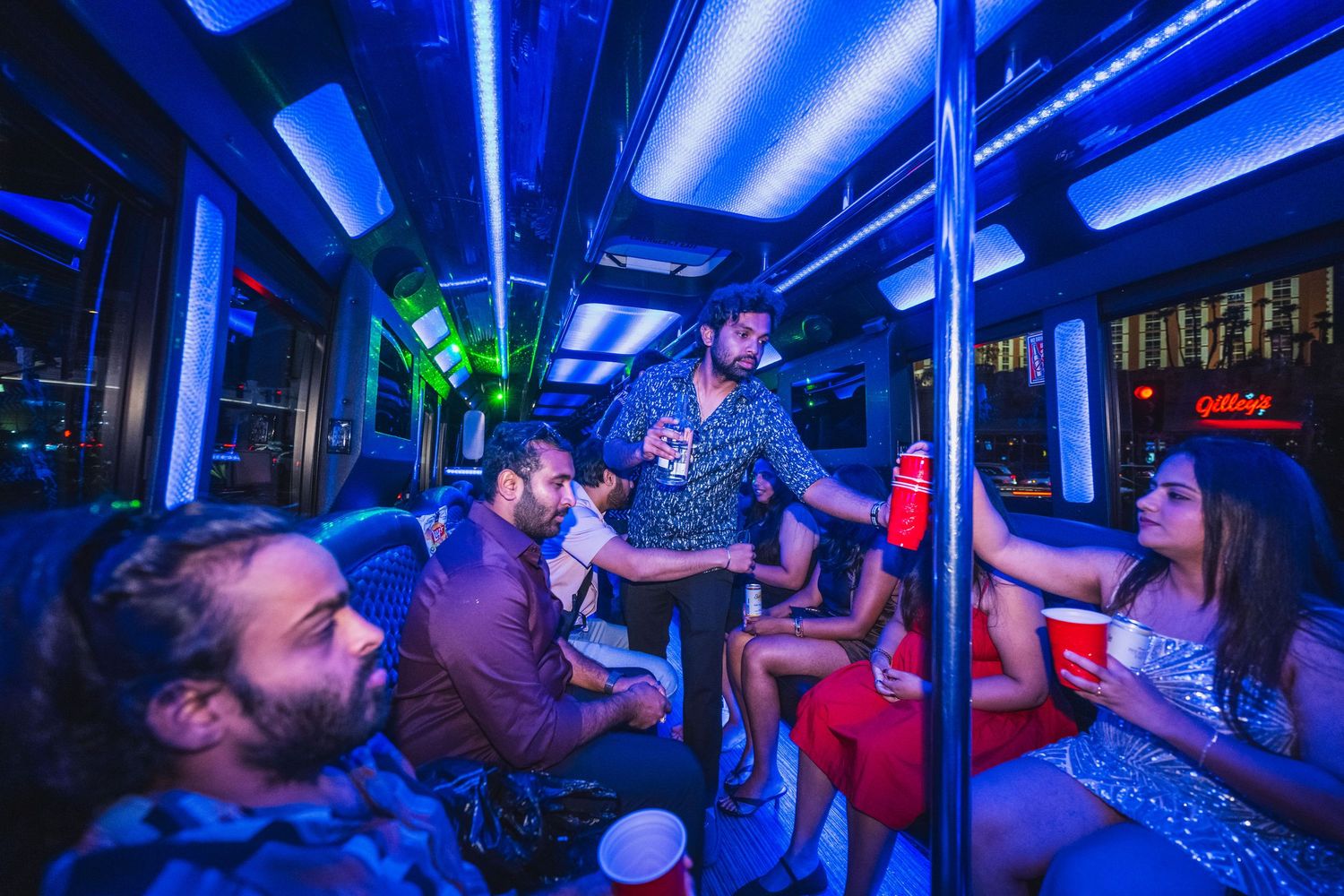 Group of friends partying inside a neon-lit party bus with red solo cups.