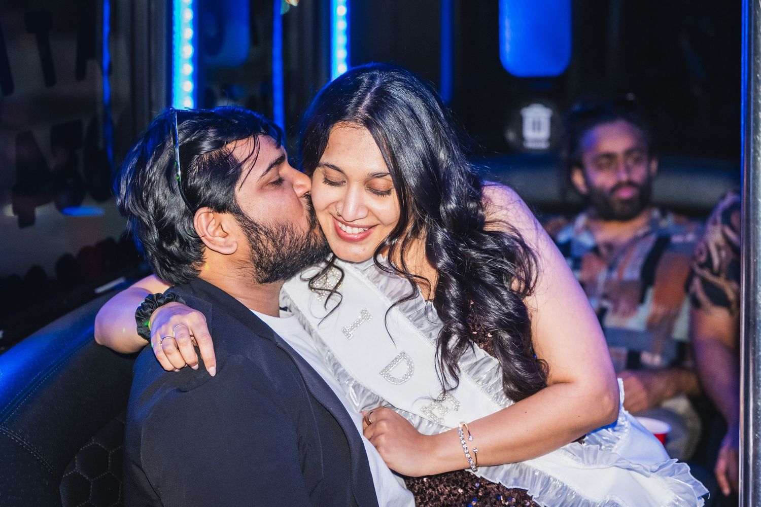 Couple sharing a romantic kiss at a vibrant nightclub party with blue LED lights.