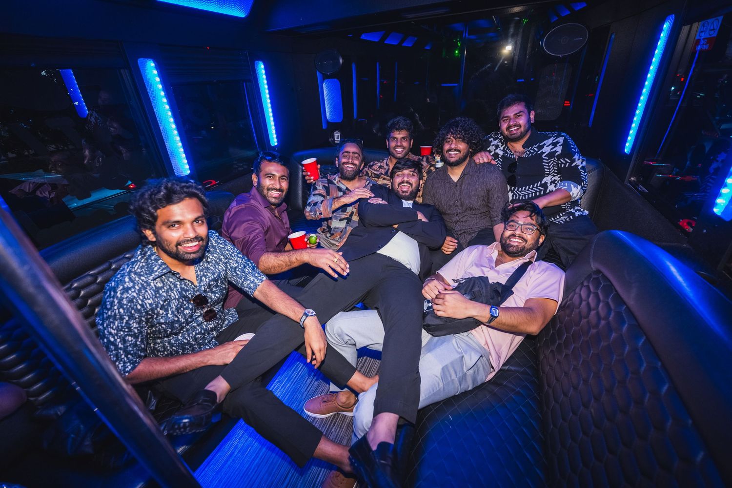 Group of men relaxing and posing together inside a blue neon-lit party bus.