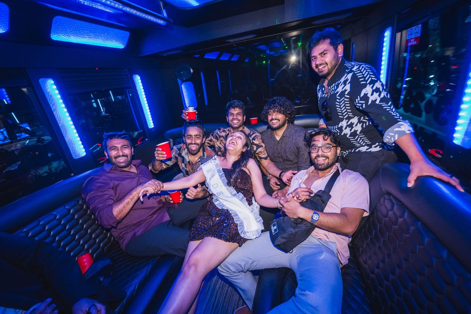 Group of friends laughing and posing together inside a neon-lit party bus.