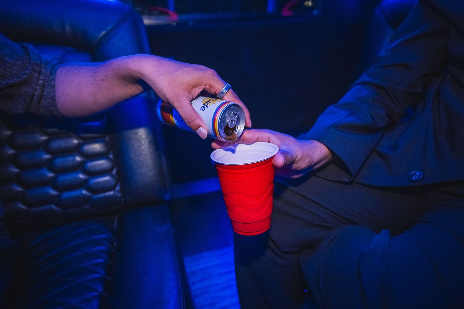Person pouring a canned drink into a red solo cup inside a dimly lit party bus.