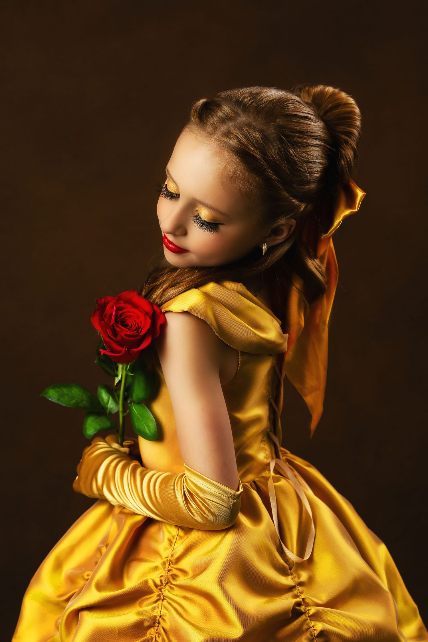 A figure in a luxurious golden ball gown holds a single red rose against a dark background in a dreamy portrait.