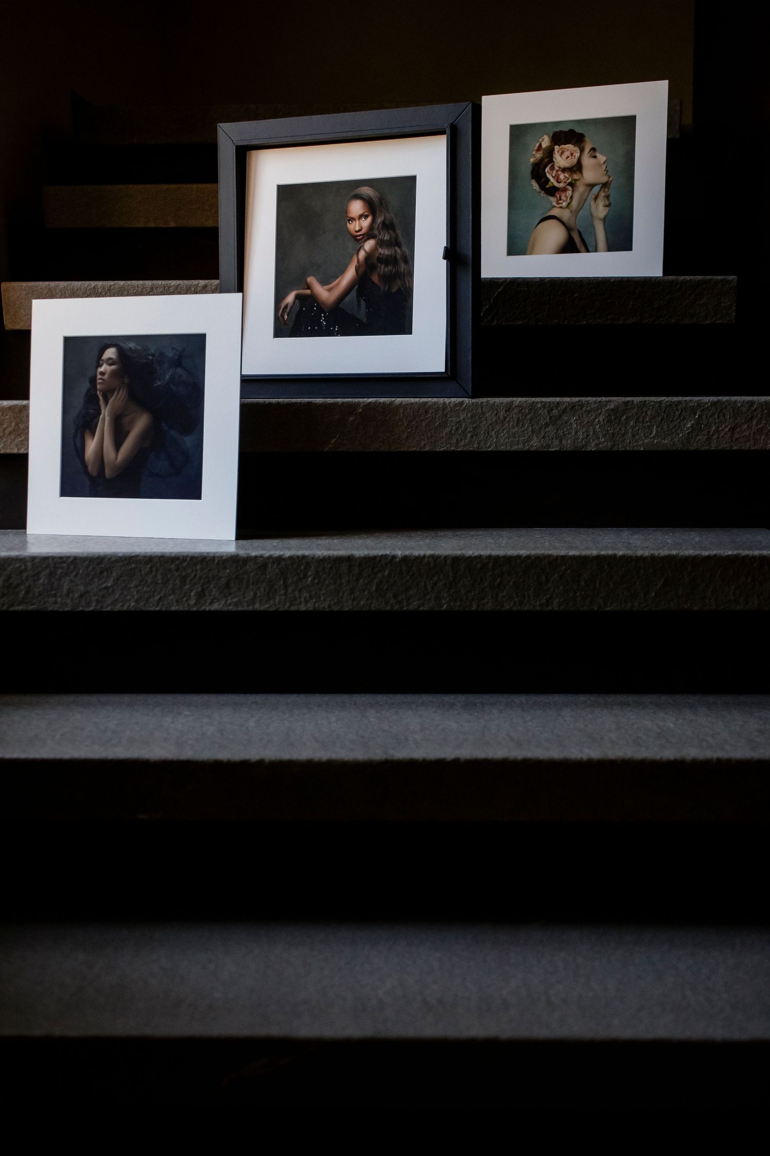 Series of black and white portrait photographs displayed in white mats against dark surface.