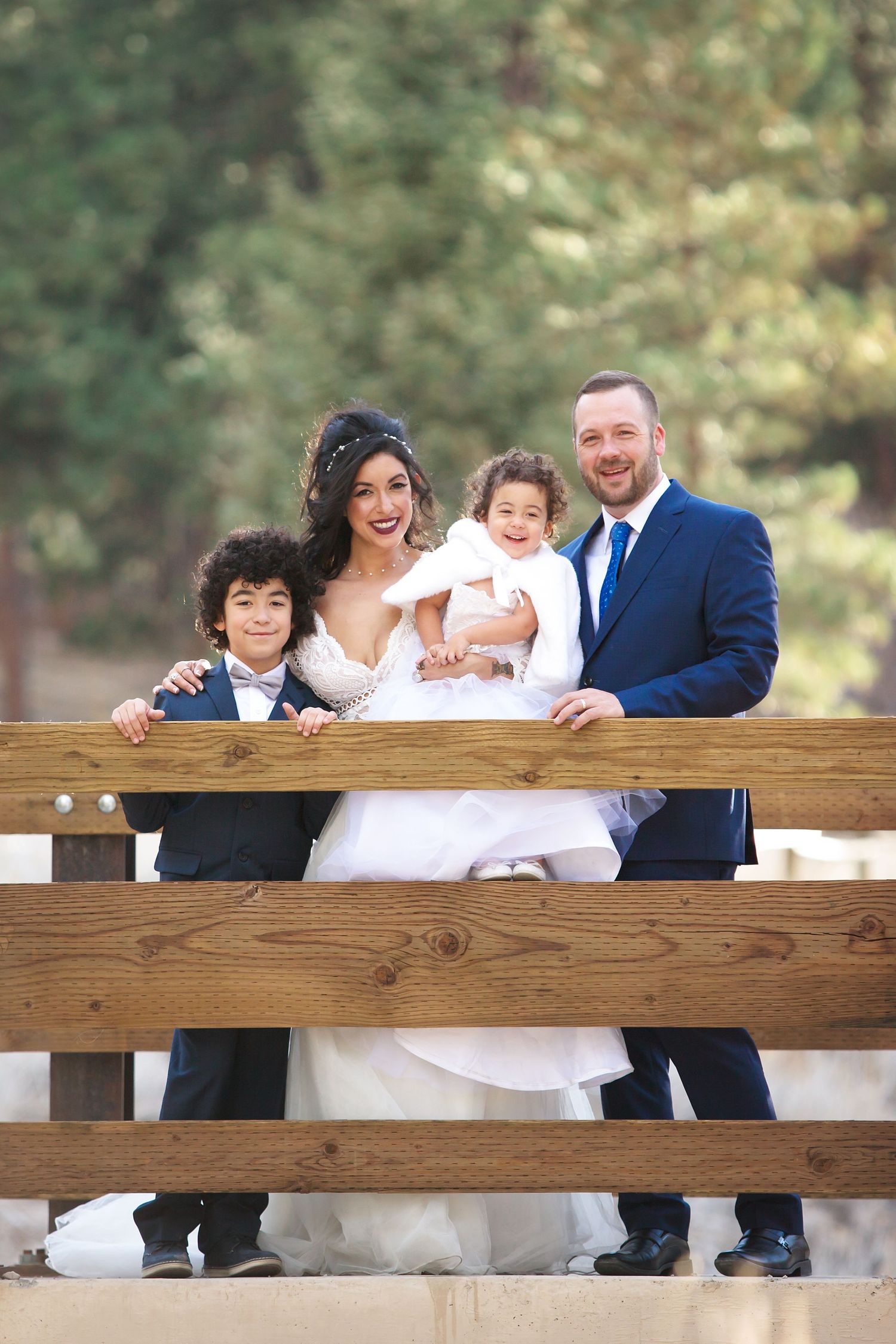Family in coordinated white and navy outfits poses together at a rustic wooden fence in an outdoor setting.