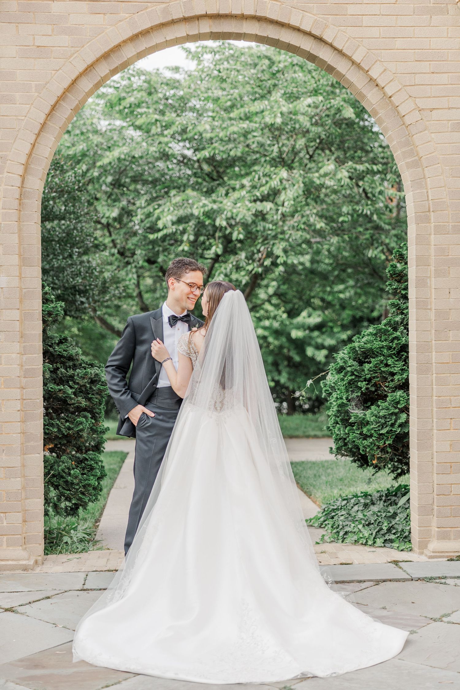Wedding couple shares romantic moments under elegant stone archways in a garden setting.