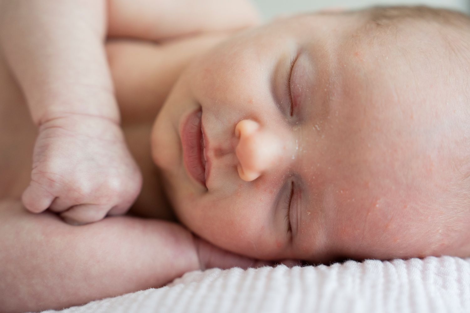 Peaceful sleeping baby rests on soft white textured blanket with delicate skin and closed eyes.