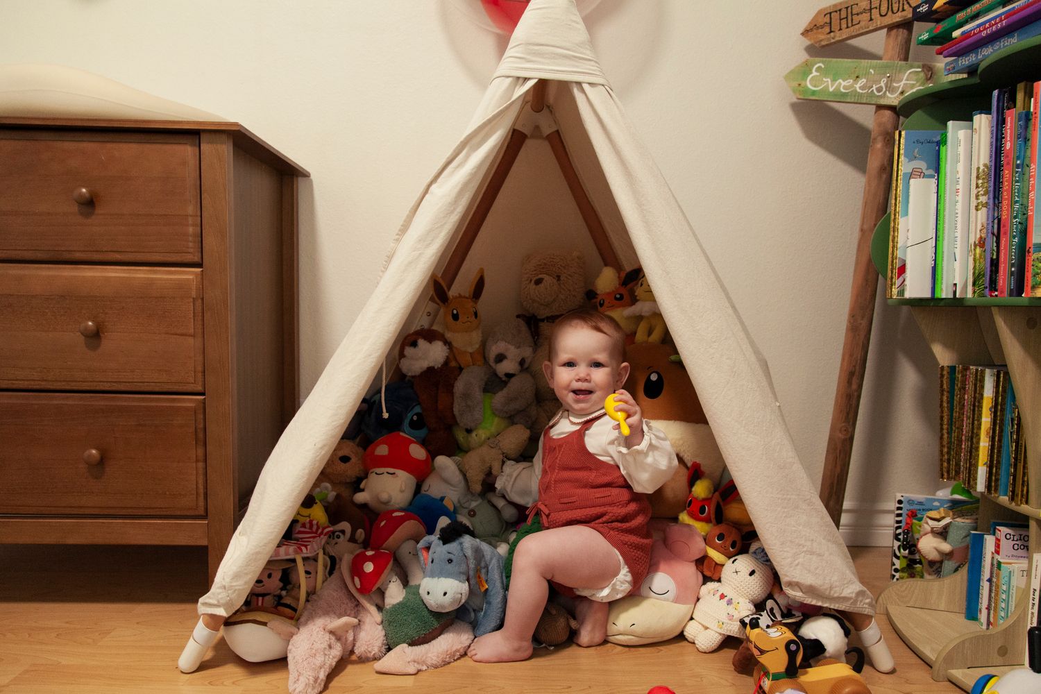 A cozy indoor reading nook with blankets, pillows, and books arranged under a tent-like structure.