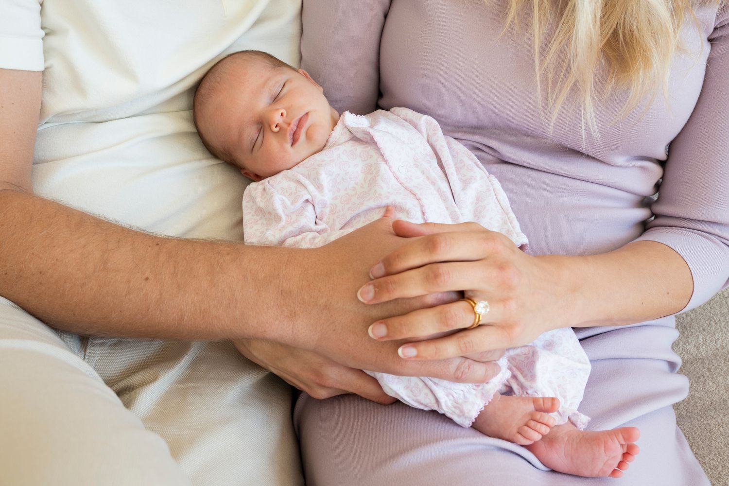 A sleeping newborn baby swaddled in white rests peacefully while being held by gentle hands.