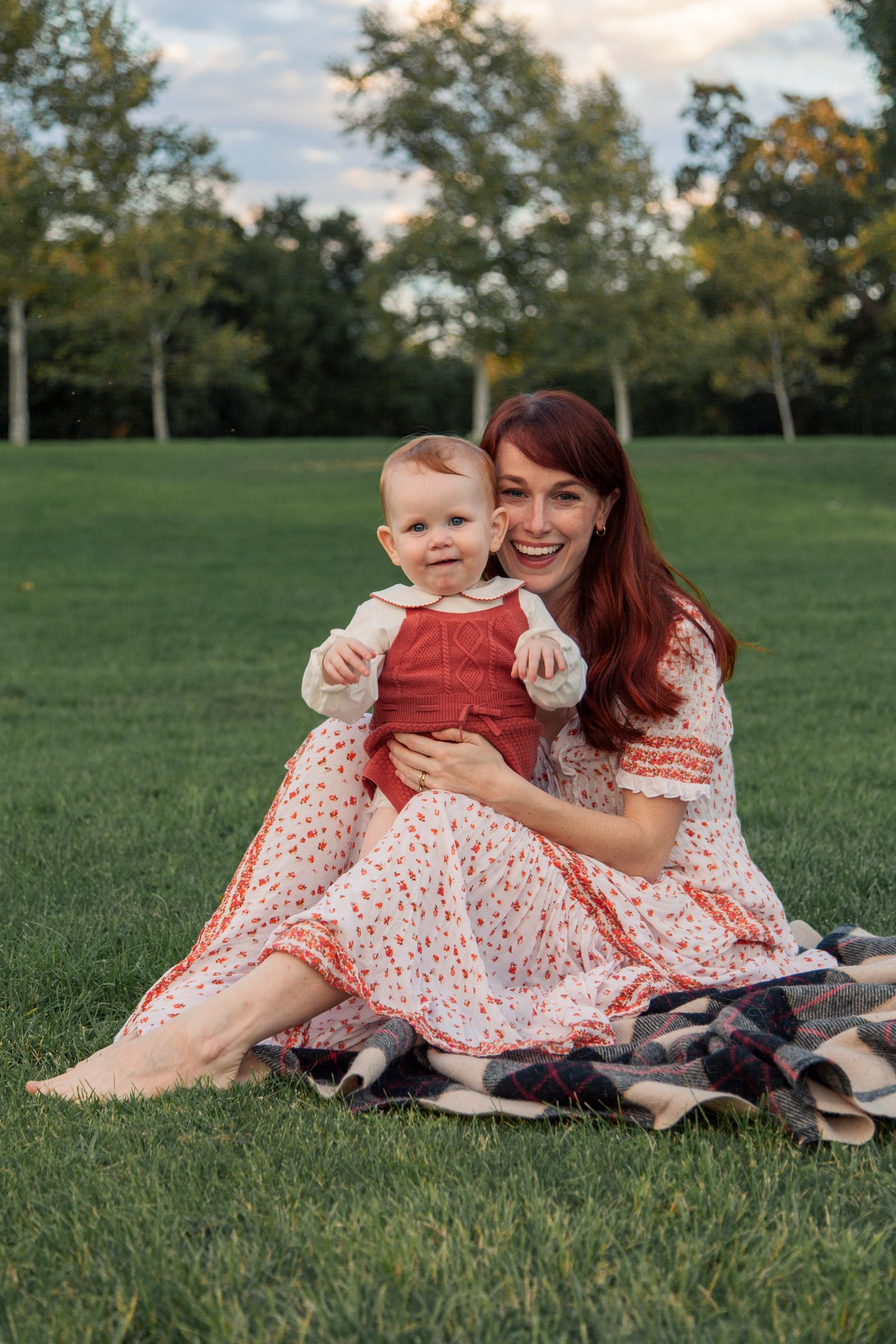 A parent and child in matching floral dresses relax together on green grass during a sunny afternoon.