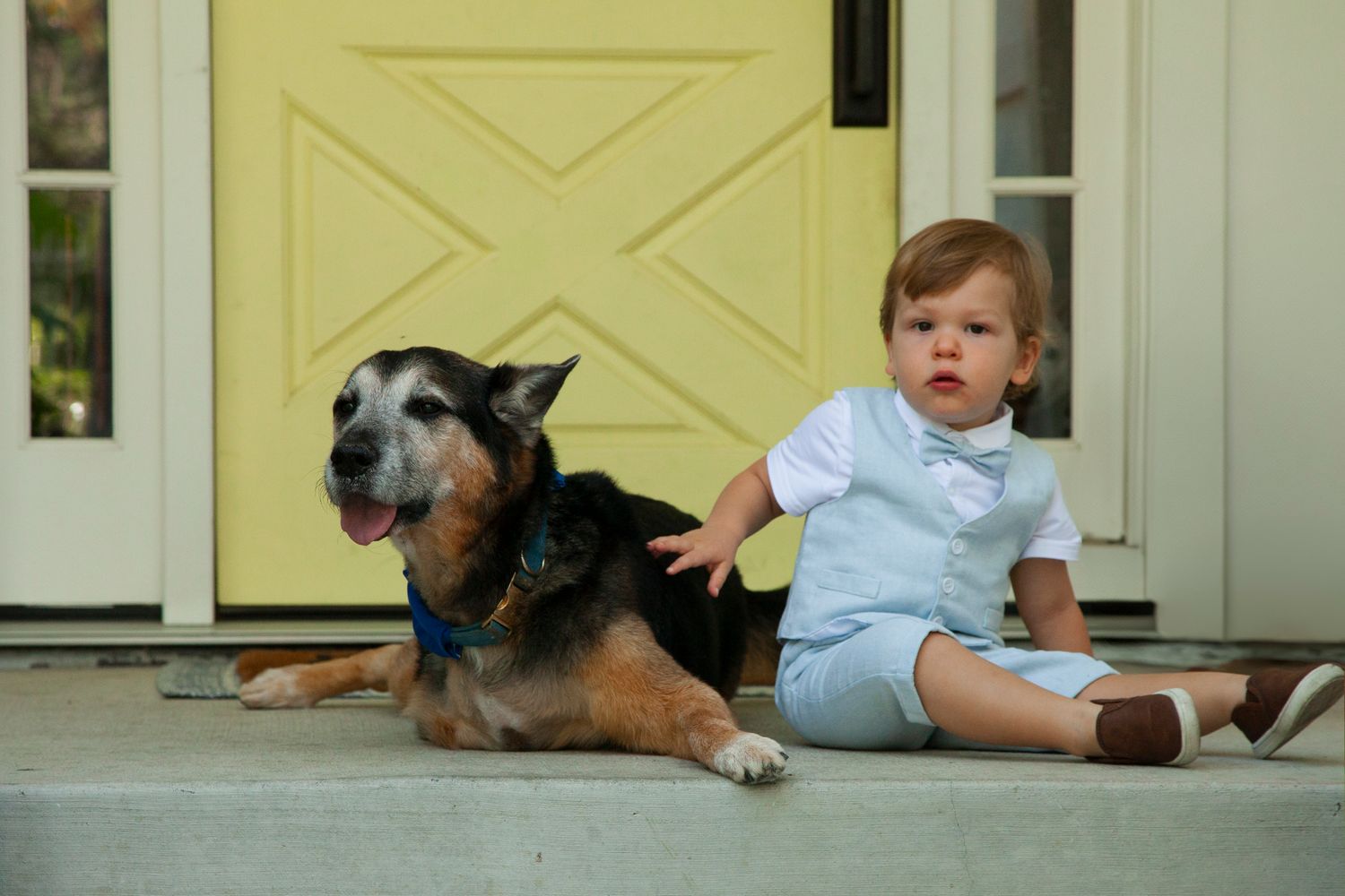 A dog and child lay together on a porch in front of a yellow door.