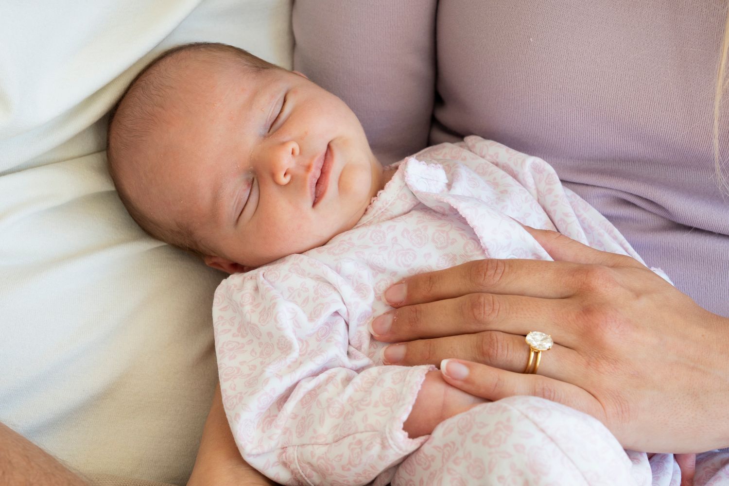 A sleeping baby wearing pink clothing rests peacefully on soft white bedding.