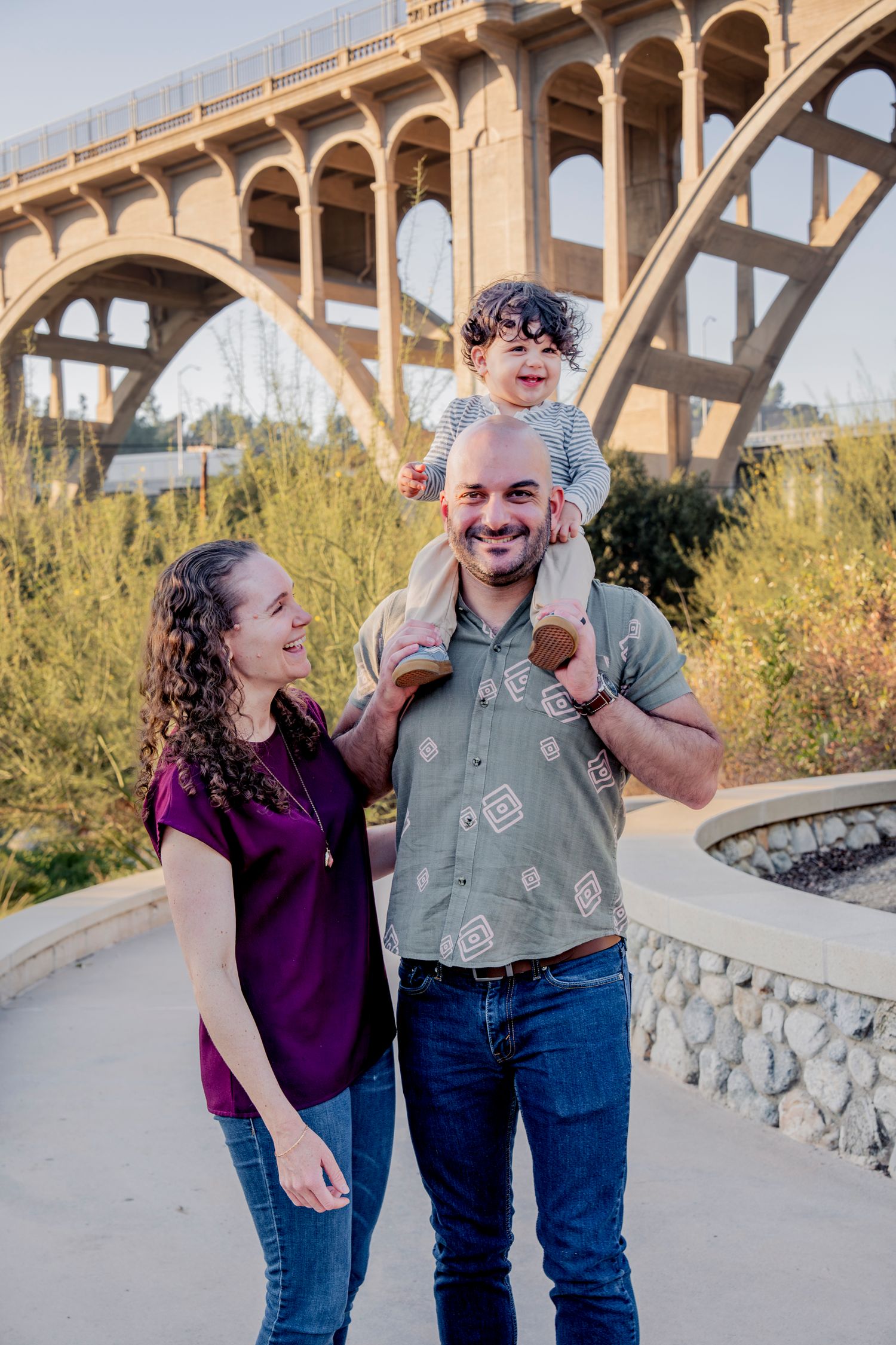 Couple laughing together during outdoor photo session under concrete bridge with desert vegetation.