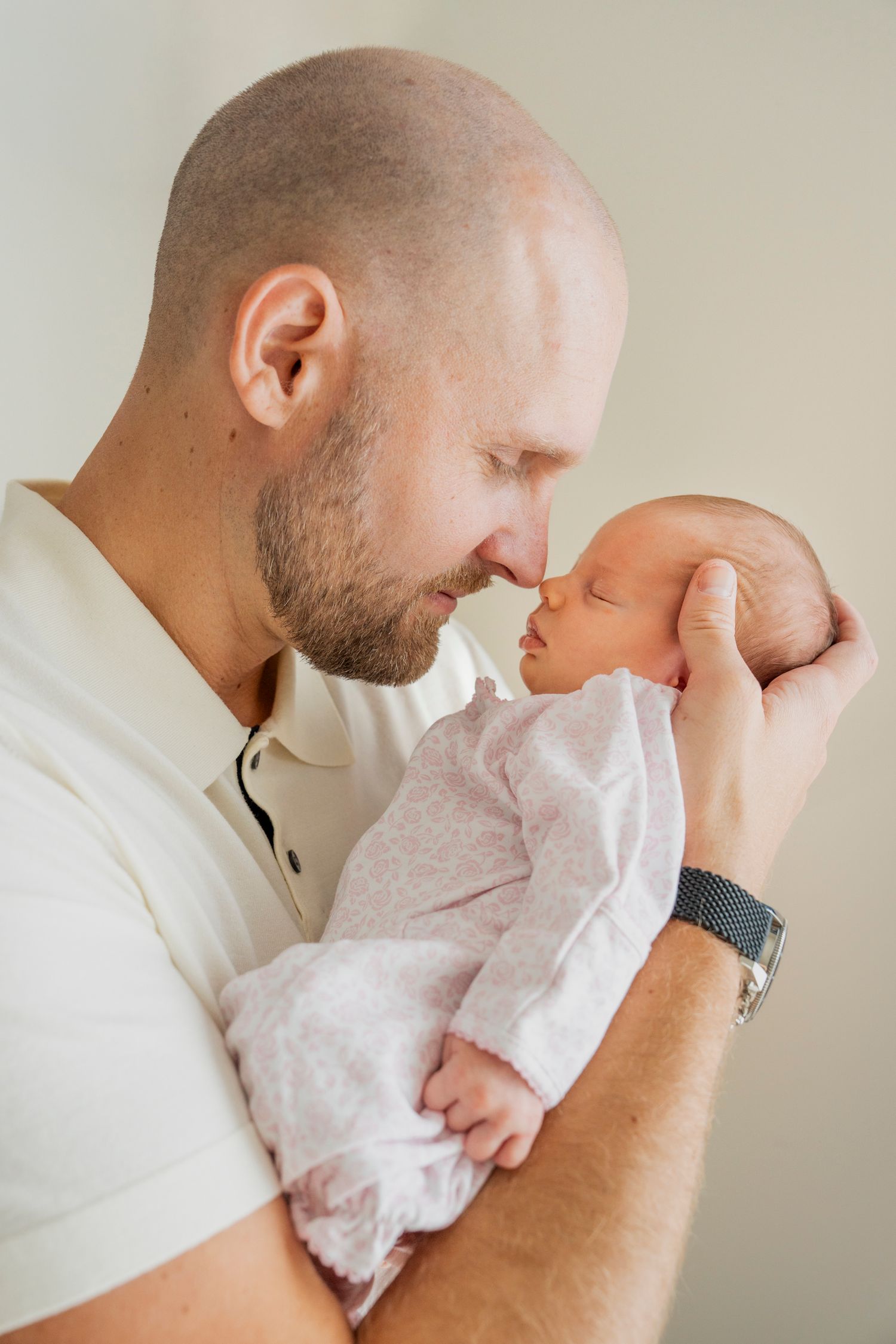 Parent in white shirt shares tender moments with newborn baby wearing delicate white dress in intimate photo series.