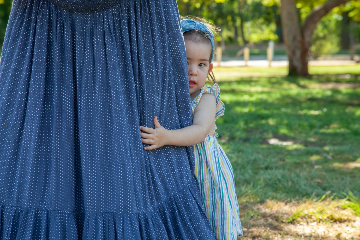 Mother and child in blue dresses walk together through a sunny park on a summer afternoon.