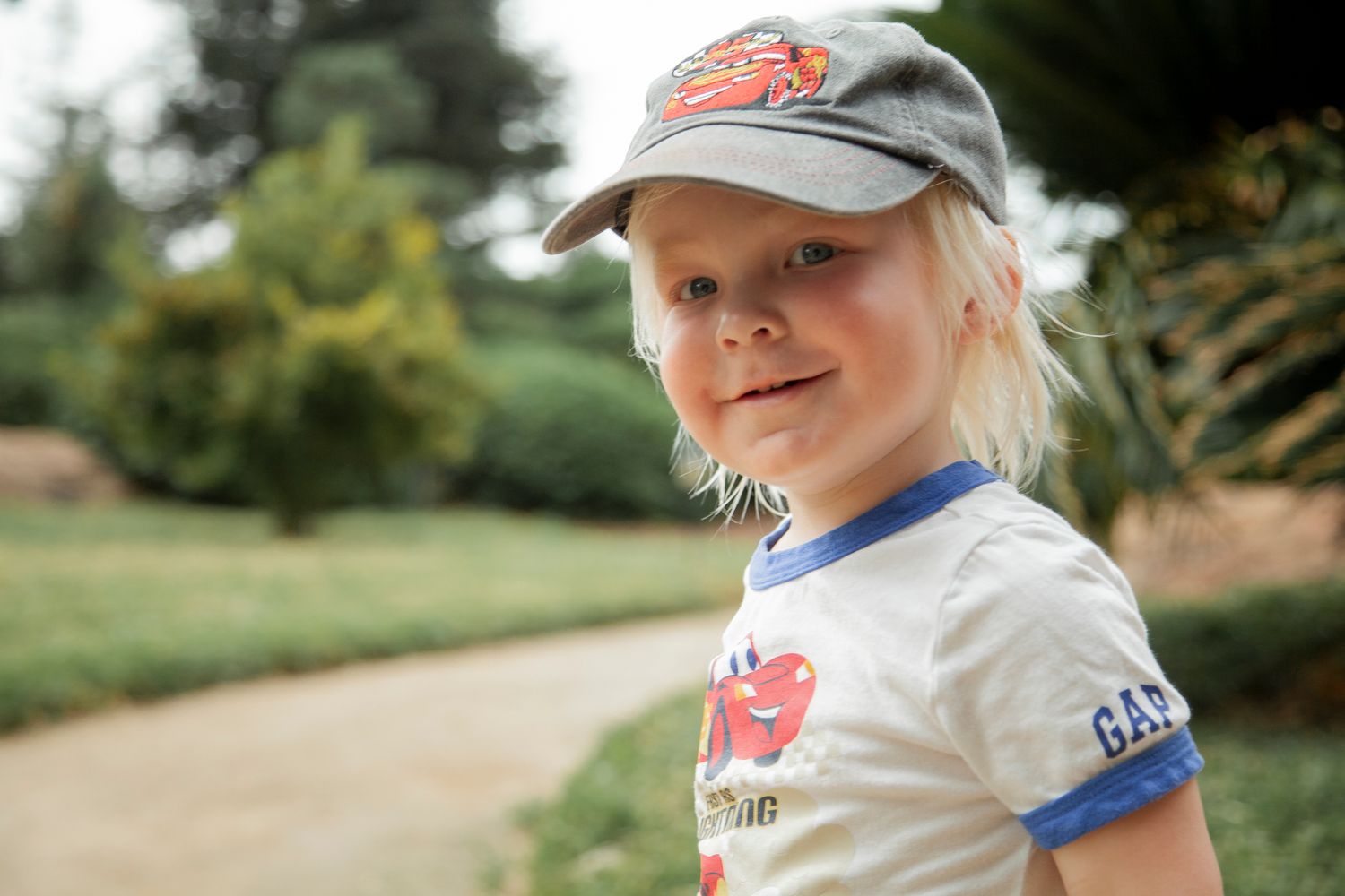 Child wearing a baseball cap playing outdoors in a natural setting.