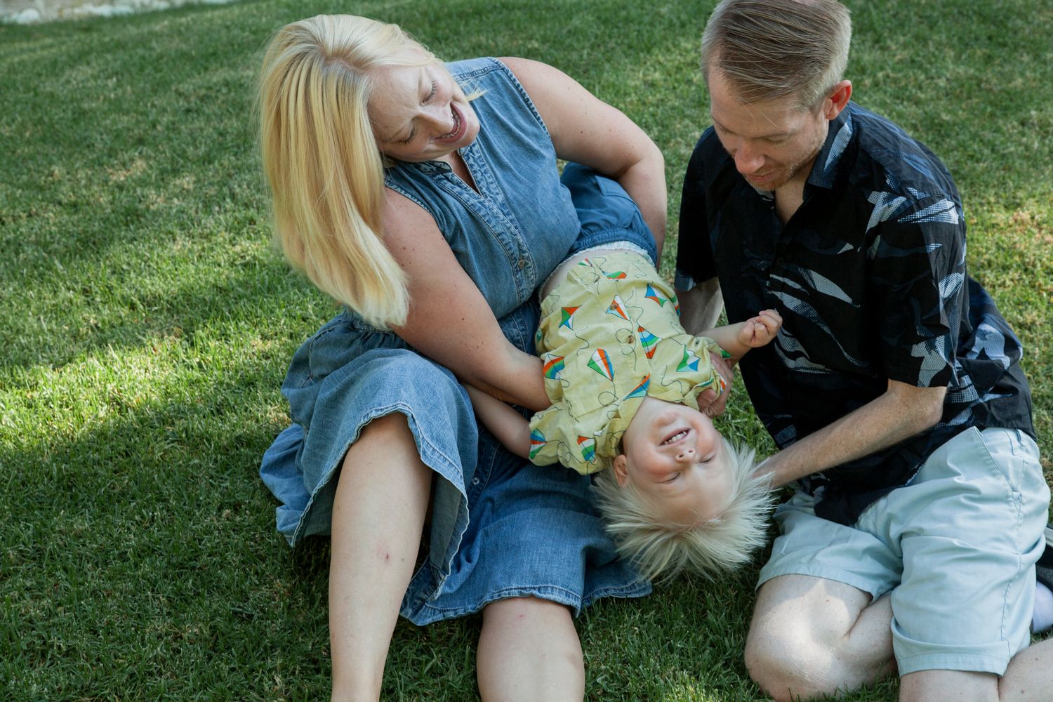 A playful sequence of people rolling and laughing together on green grass in summer.