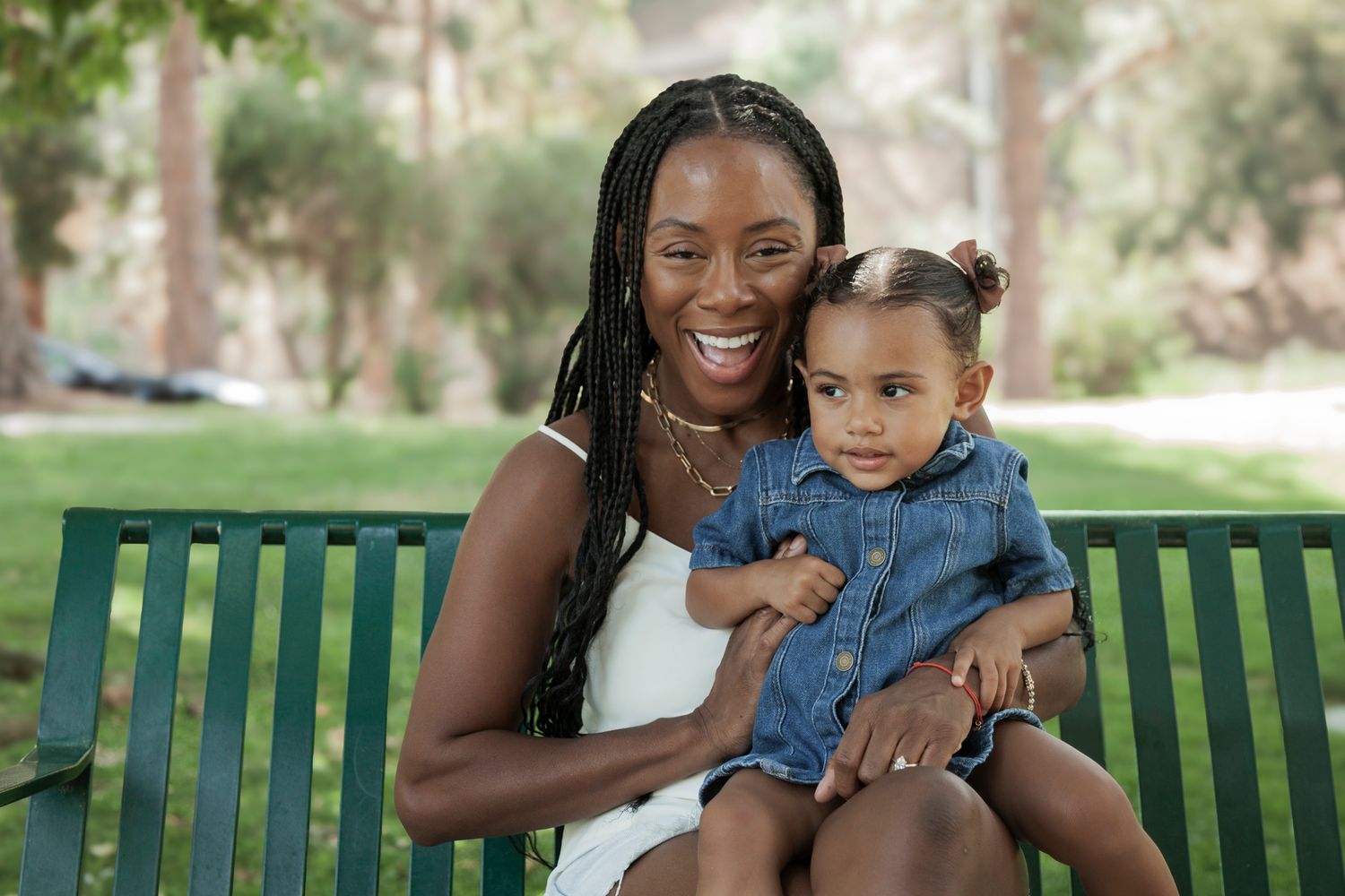 A joyful family moment captured on a green park bench during a sunny outdoor photo session.