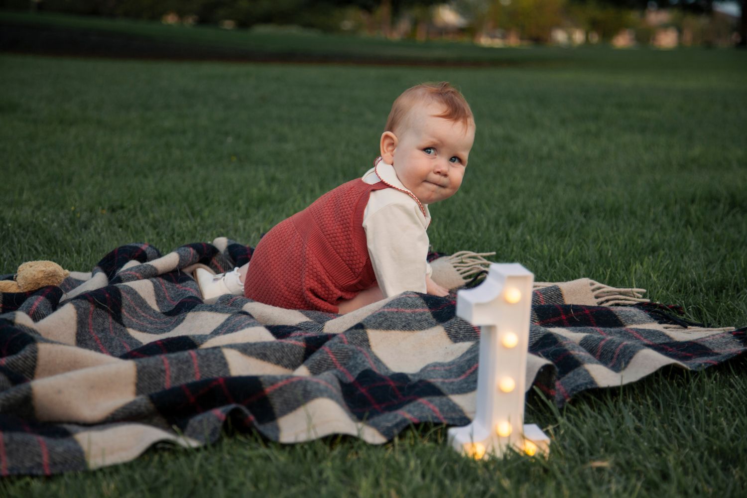 A person lying on a patterned blanket in green grass during a sunny day.