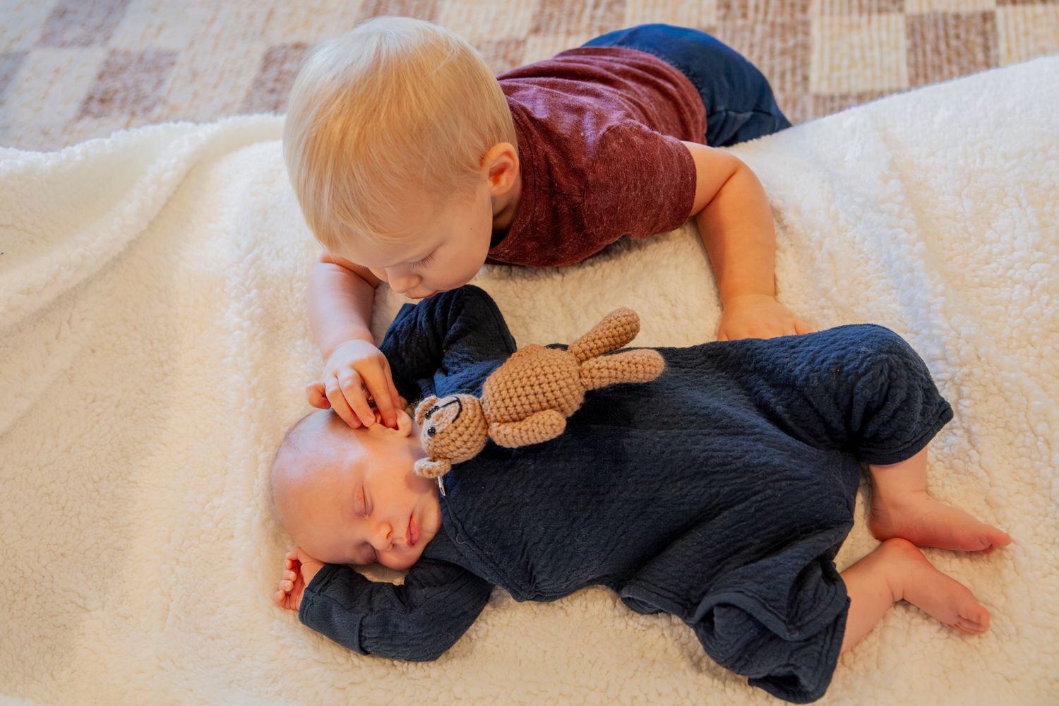 A baby in a navy blue outfit lies on a beige carpet while rolling and playing on their back.