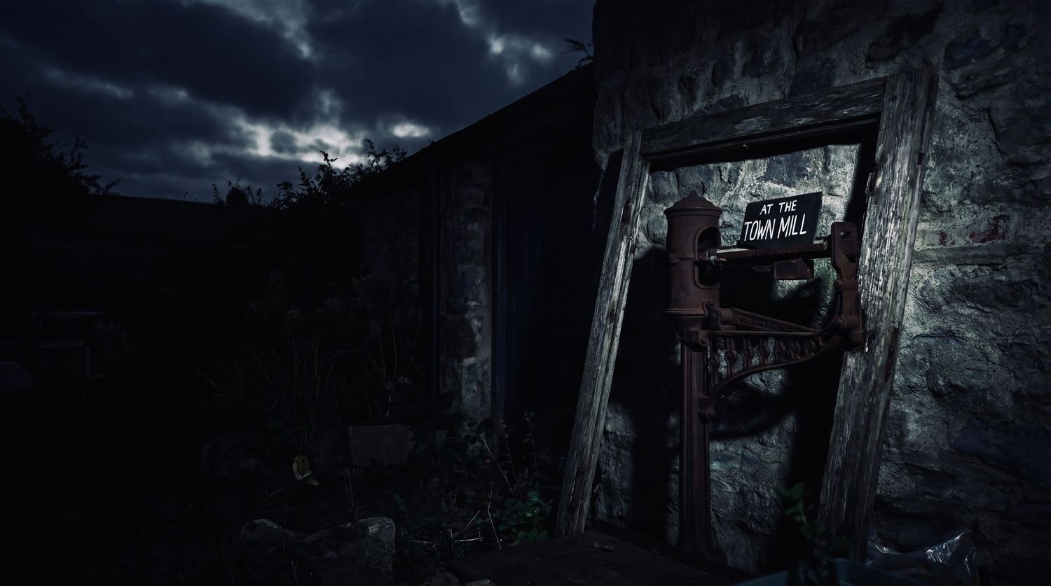 Dark atmospheric scene of a figure standing in a stone doorway at night with dramatic cloudy sky.