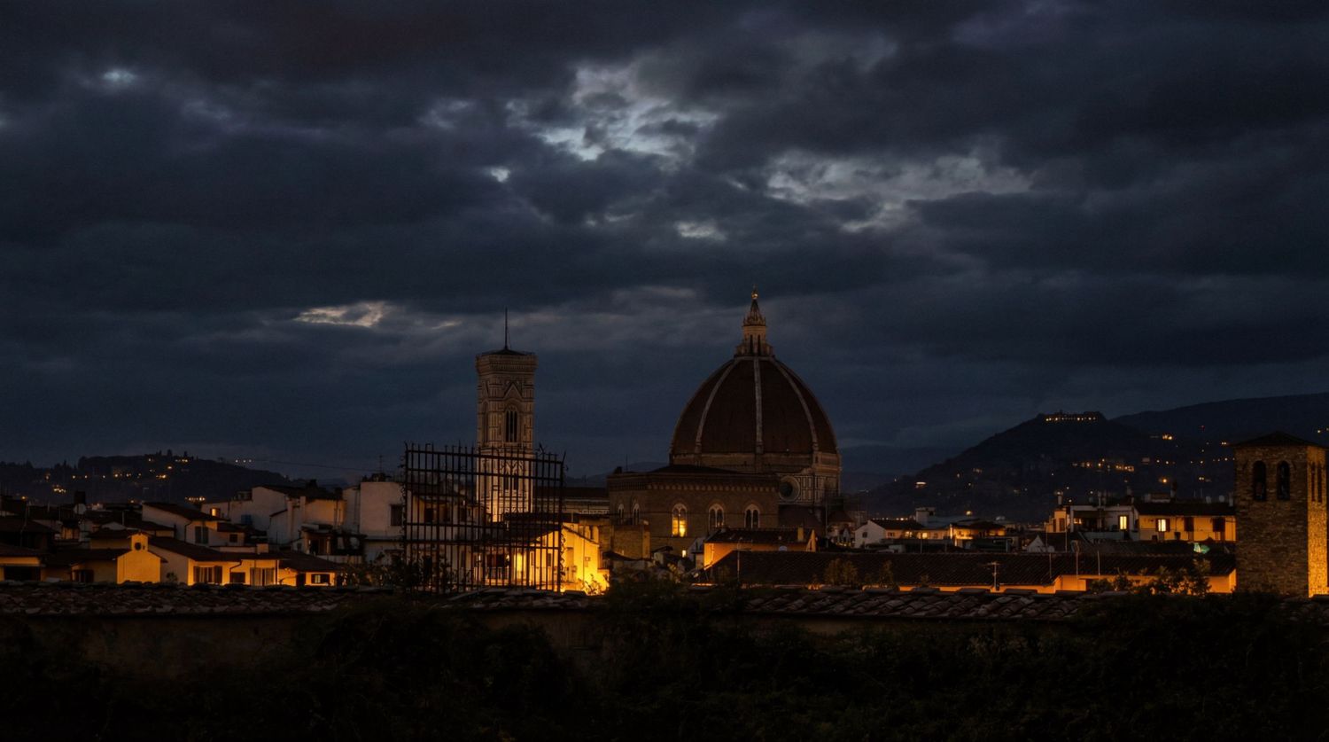 Dramatic panoramic cityscape of Florence Italy at dusk with illuminated Duomo cathedral under stormy clouds.