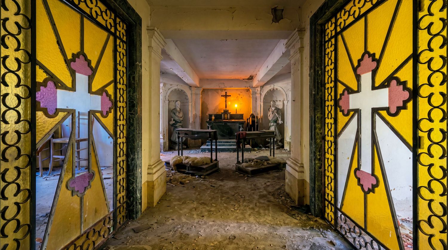 Abandoned church interior with ornate stained glass doors featuring crosses, leading to a dusty altar with candlelight.