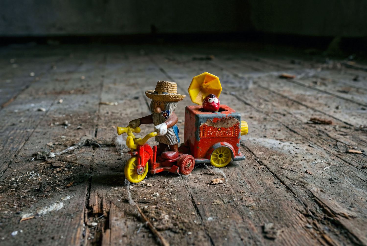 Vintage toy monkey riding a red tricycle pulling a small wagon on a weathered wooden floor.