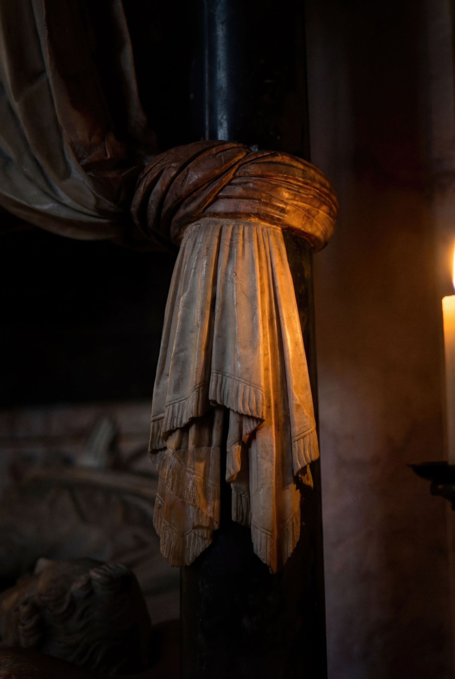 Draped fabric illuminated by warm candlelight creates dramatic shadows and folds in a dark atmospheric setting.