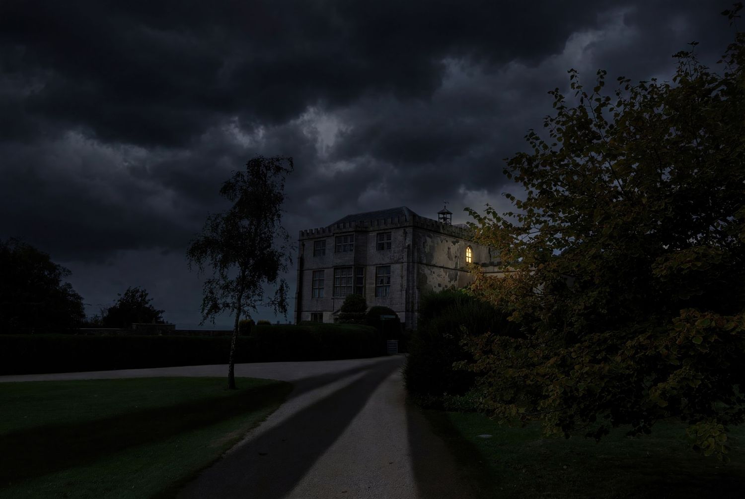 Dark storm clouds loom over a rural landscape with silhouetted trees and buildings at dusk.