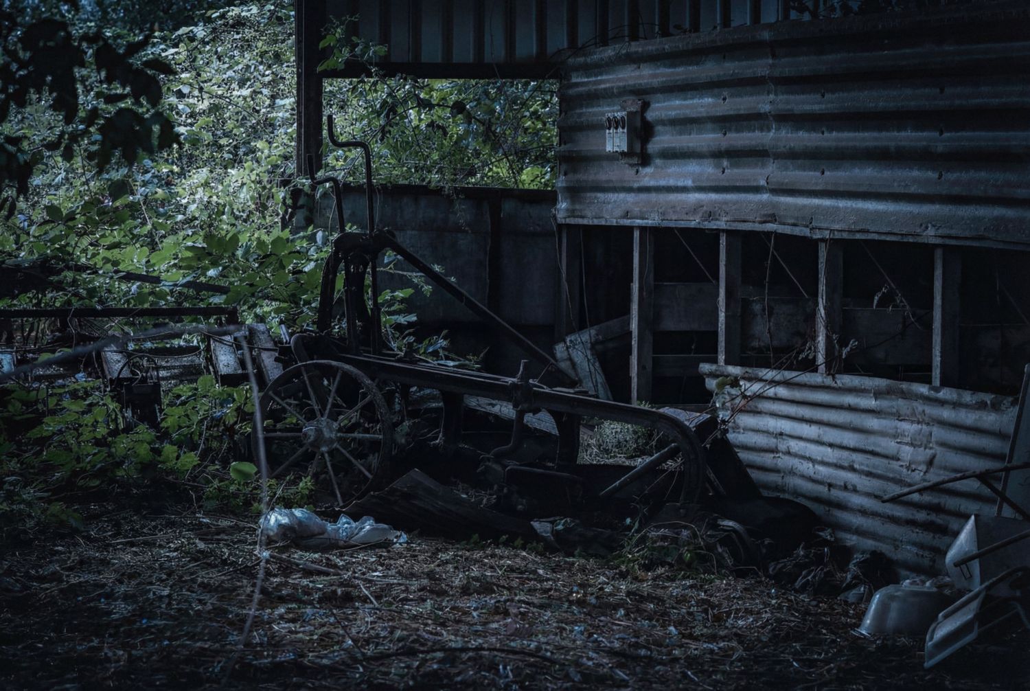 A series of rustic wooden sheds and outbuildings stand among trees and foliage in a rural setting.