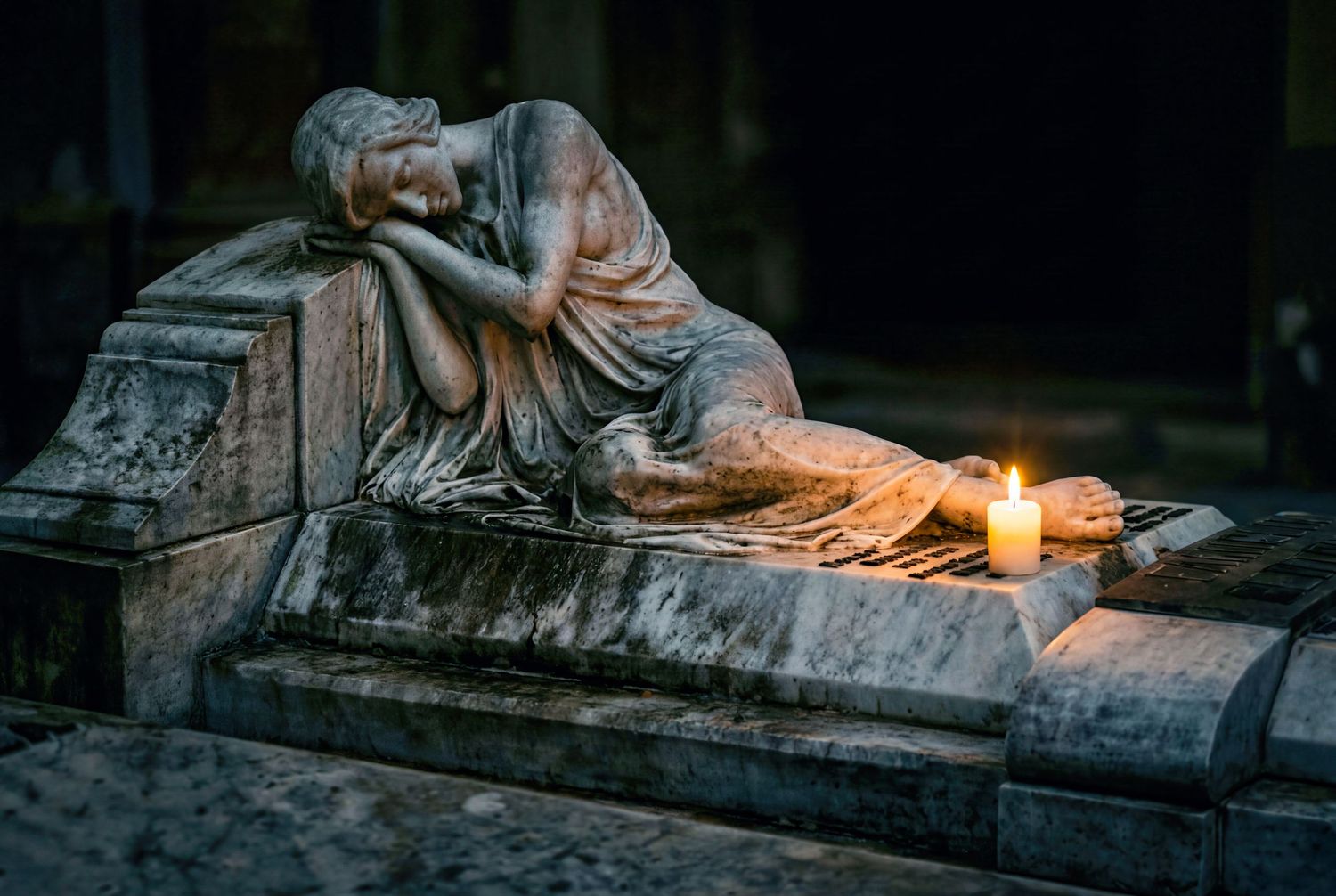 Stone sculpture of a grieving woman reclining on a tomb with a lit candle glowing softly in the dark.