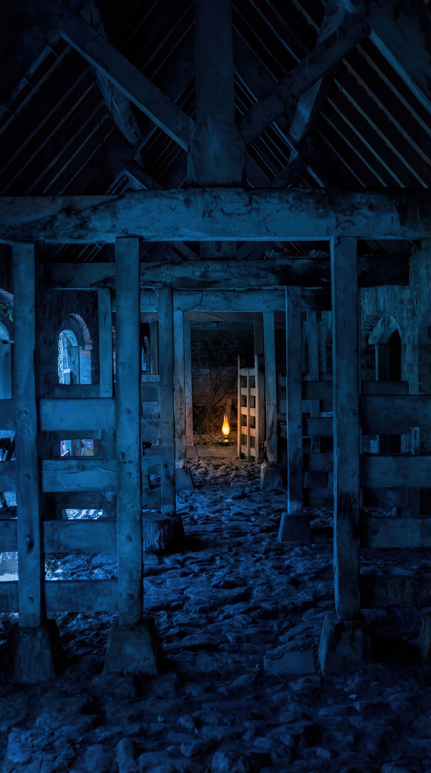 Eerie blue-lit abandoned industrial interior with stone pillars and debris-strewn floor leading to a distant illuminated doorway.