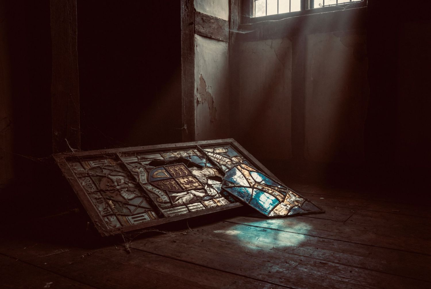 Sunlight streams through a window into a dark, abandoned room creating dramatic shadows on the wooden floor.