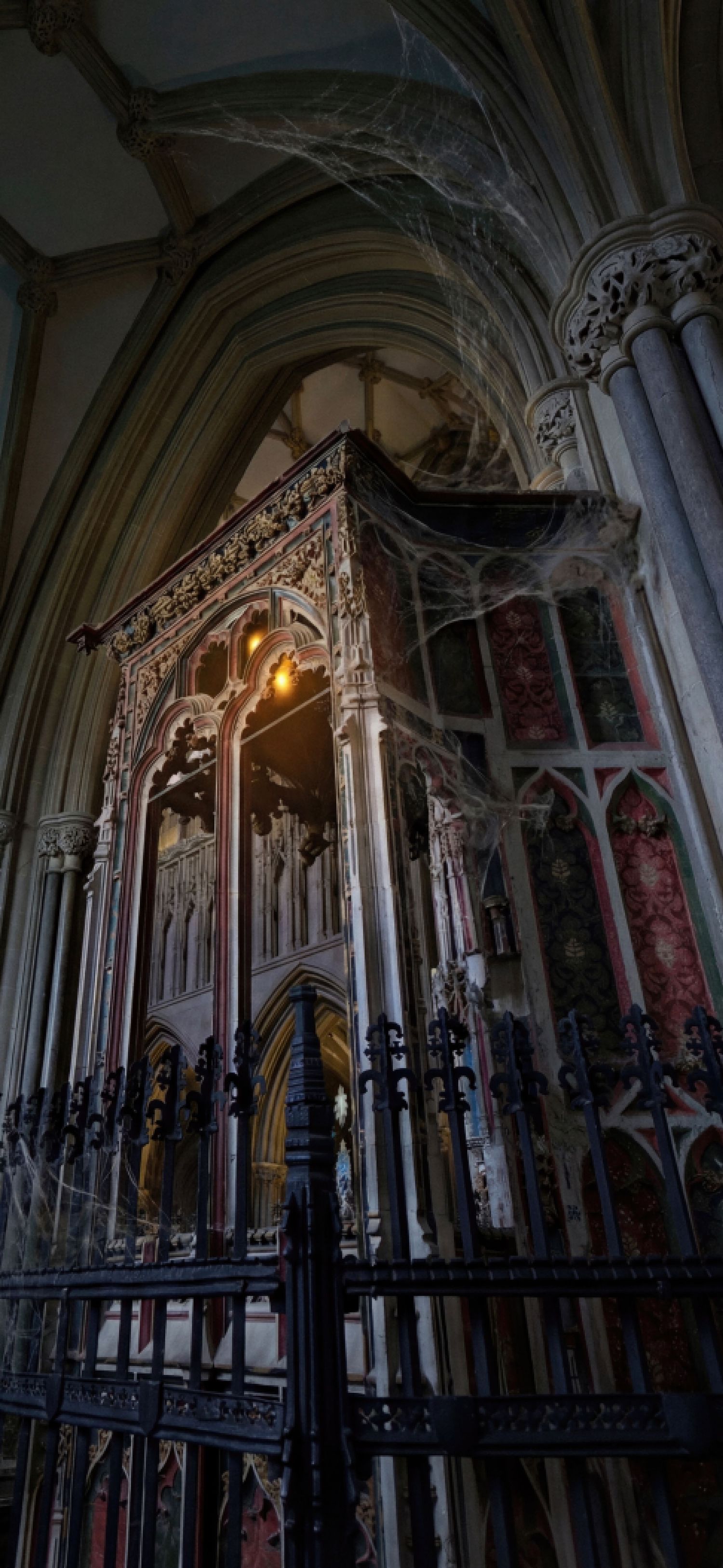 Gothic cathedral interior with ornate carved stone archways and spooky cobwebs in dim lighting creating a haunting atmosphere.