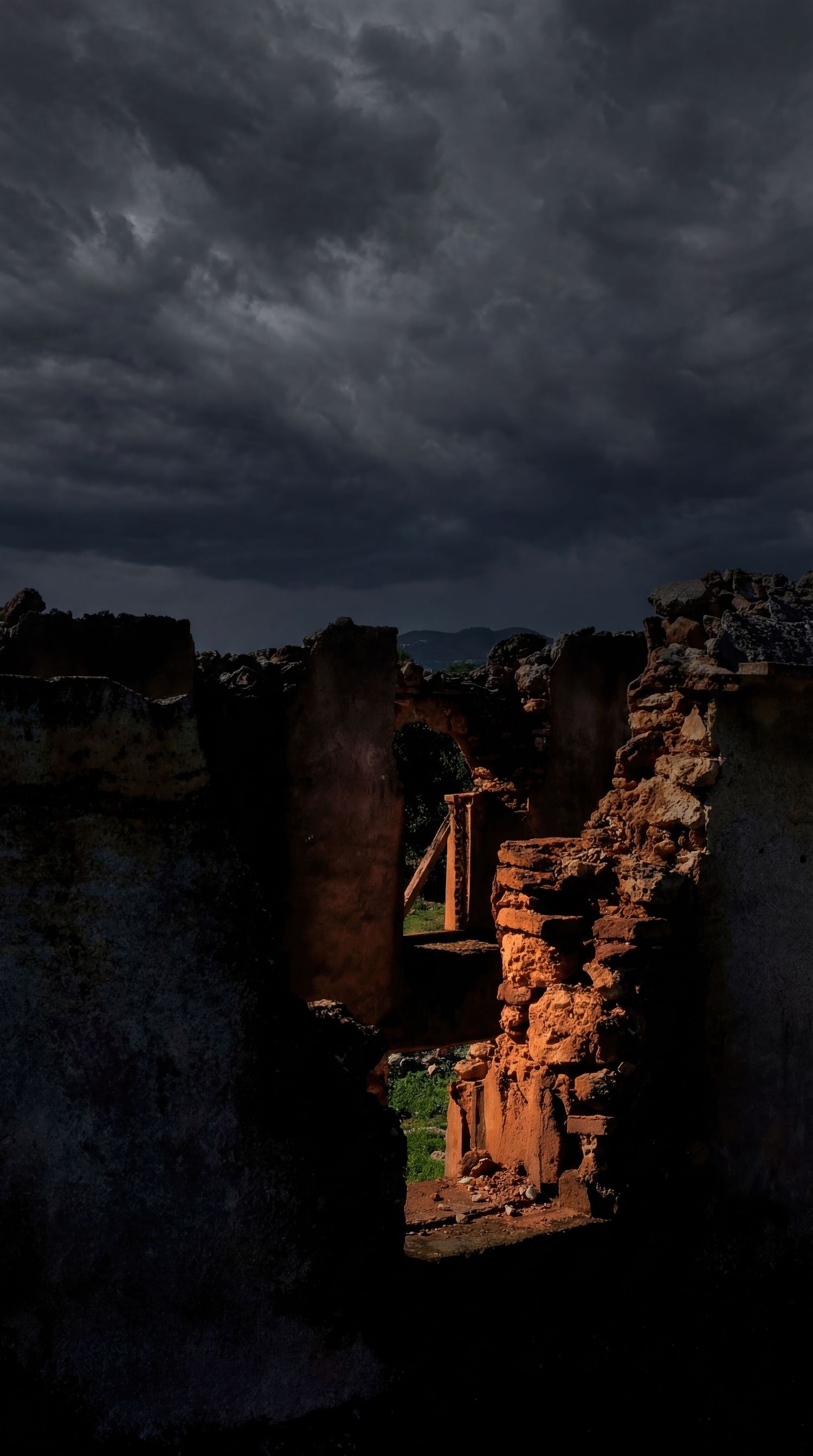 Ancient cliff dwellings stand against a dark stormy sky in a dramatic desert landscape.