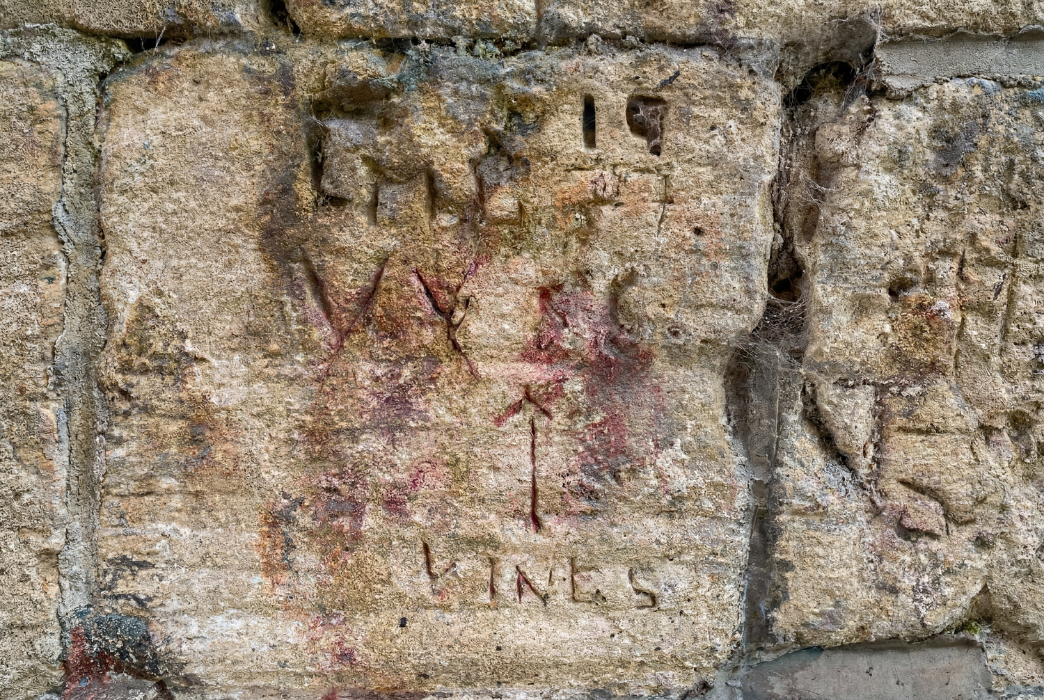 Ancient stone wall with carved inscriptions and red painted letters, including the word VINES, on weathered limestone blocks.