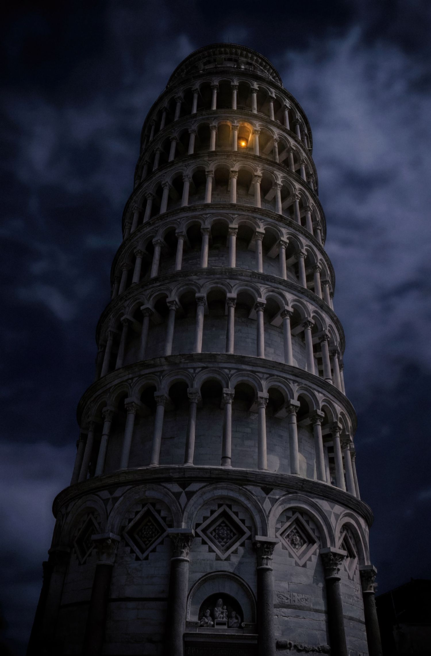 The Leaning Tower of Pisa photographed at night against a dark cloudy sky with dramatic lighting and shadows.