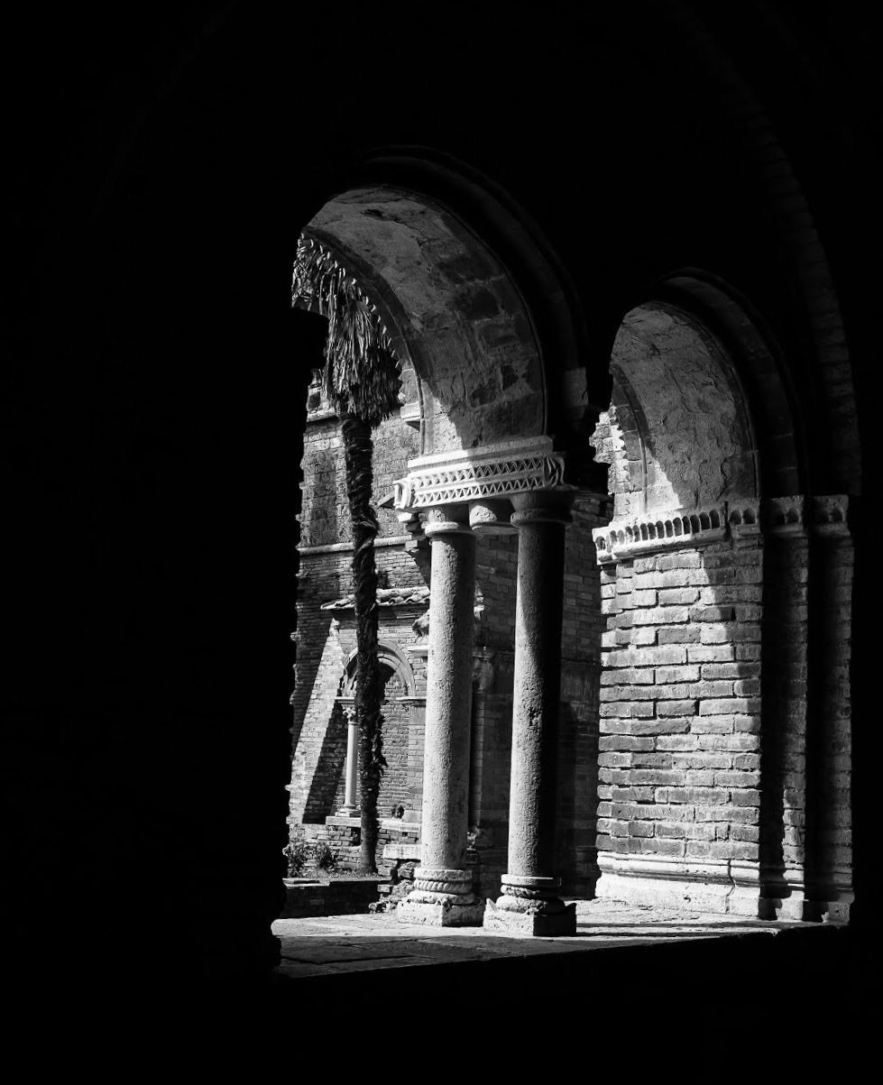 Black and white photo of ancient stone arches and columns in a historic ruins, dramatic contrast highlighting architectural details.