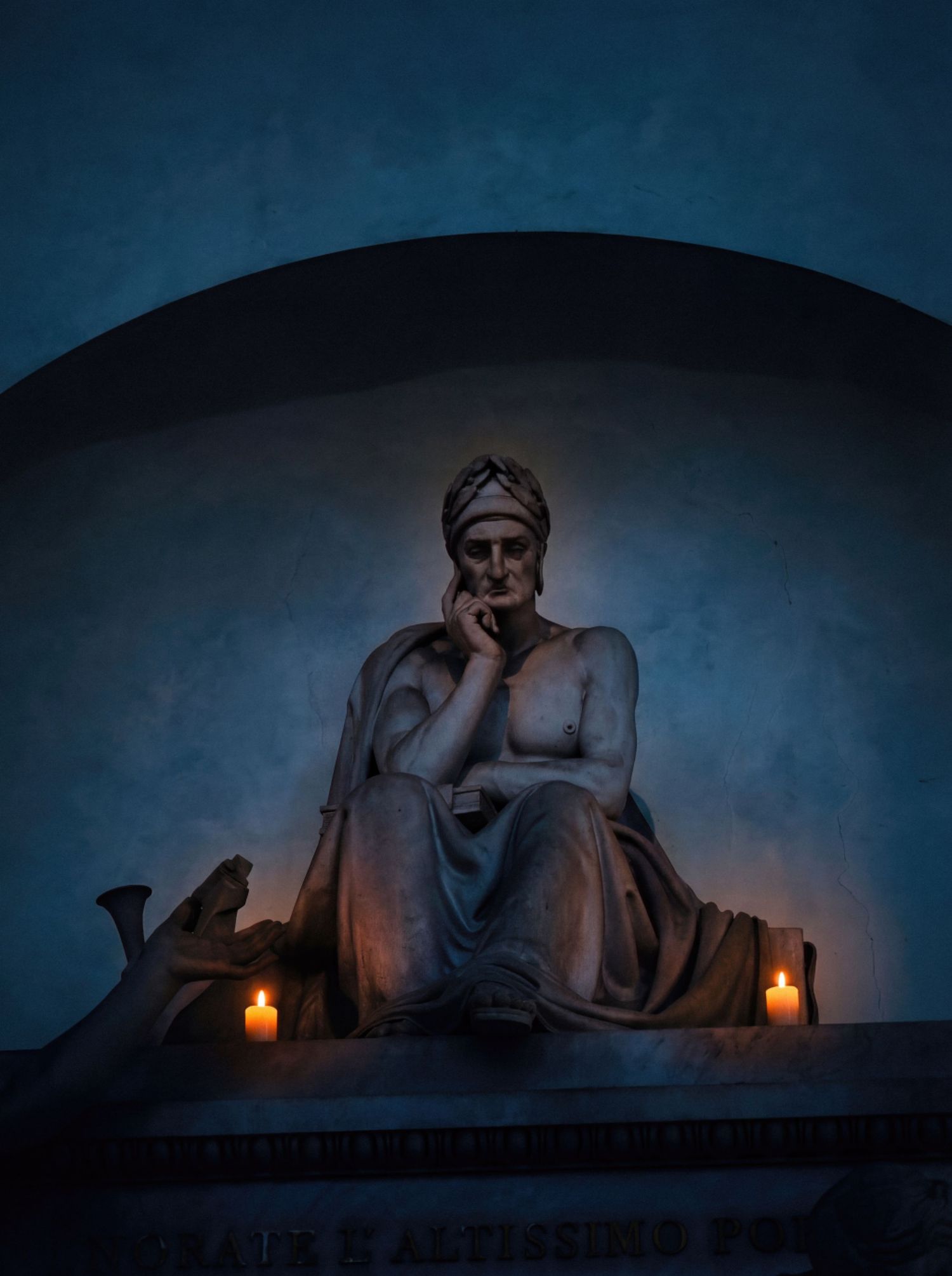Stone sculpture illuminated by candlelight at night creates a dramatic and moody atmosphere against dark blue sky.