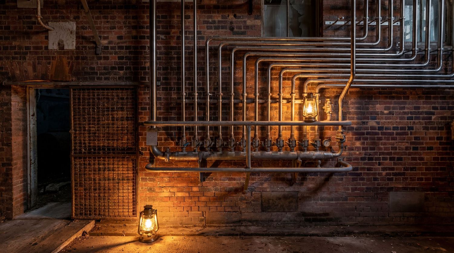 Vintage industrial brick wall with metal pipes and glowing lanterns casting warm light in a dark basement.