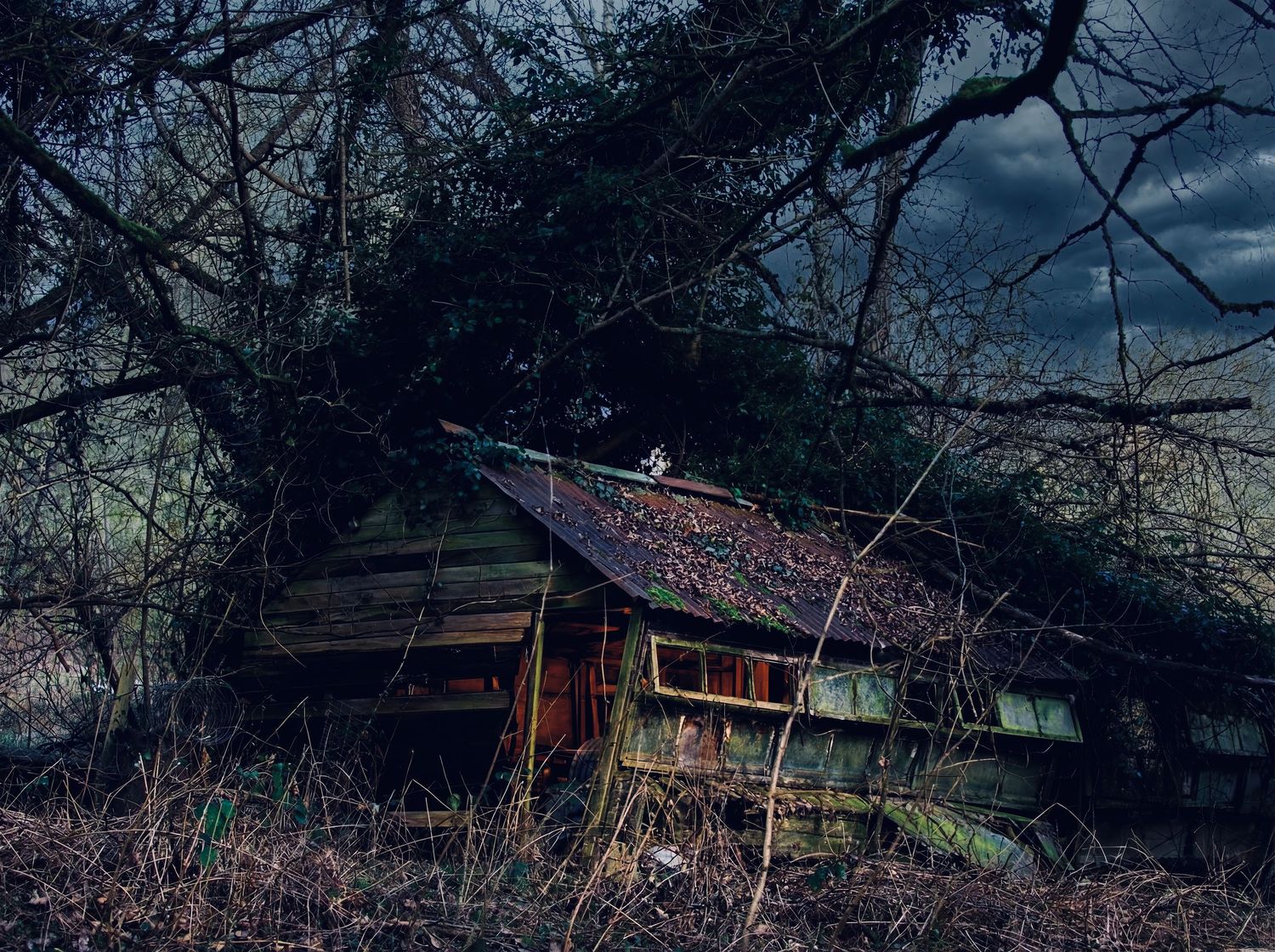A dark and moody winter landscape features snow-covered trees and rustic cabins at twilight.