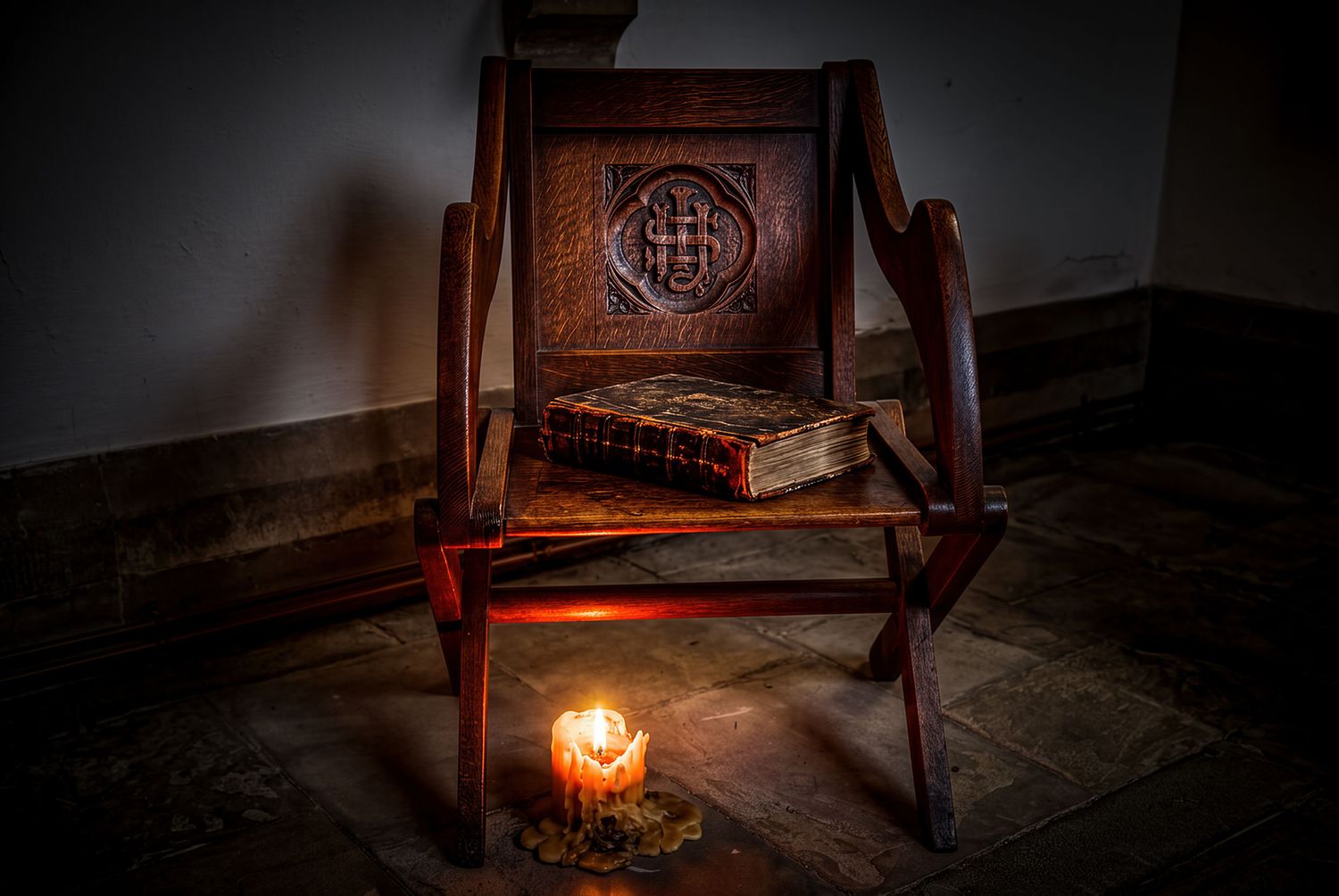 Antique carved wooden chair with an old book on the seat, illuminated by a single candle on a stone floor.